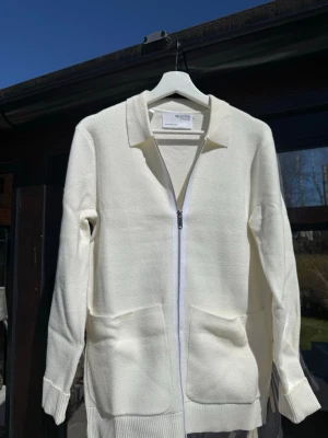 Vit ziptröja från Selected Homme - Stilren vit ziptröja från Selected Homme med krage och två stora fickor framtill. Tröjan är rak i modellen, har långa ärmar och ribbade muddar. Perfekt för en clean och enkel look. Storlek S och perfekt skick. Skriv vid frågor!