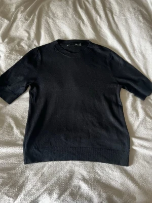 Svart stickad topp  - Snygg svart stickad topp från 157 med rund halsringning och halvlånga ärmar. Ribbstickade detaljer vid hals, ärmslut och nederkant.