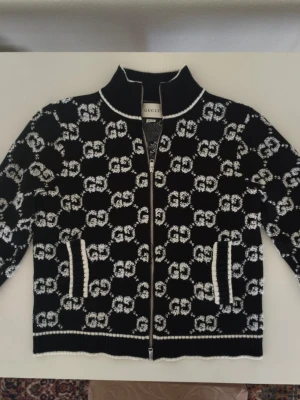 Gucci - Gucci Stickad Kofta i 100% Ull – Storlek M Säljer en stilren kofta från Gucci med det klassiska GG-monogrammet i svart och vitt. Koftan är i size medium men den kan va pyte lite mindre än storlek M. Detaljer: Material: 100% ull enligt tvättlappen, vilket gör den väldigt varm och skön. Skick: Mycket gott skick, väl omhändertagen. Storlek: Medium (M). Ursprung: Tillverkad i Italien. Varför köpa denna? Koftan har en fantastisk detaljrikedom därpå är du den ända i Sverige med den äkta koftan
