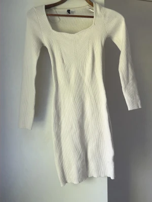 Vit ribbad långärmad klänning - Säljer en vit ribbad klänning med lång ärm och fyrkantig ringning. Klänningen är figurnära och har en kort längd, perfekt för dig som gillar en enkel men stilren look. Materialet är stretchigt och bekvämt.