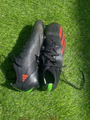 Retro Adidas X Speedportal Elites  - Snygga fotbollsskor från Adidas i svart med klassiska röda stripes på sidorna och gröna detaljer vid hälen. Skorna har snörning och mönstrad sula för bra grepp på planen. Ovandelen är i syntetmaterial och designen är smal och sportig.