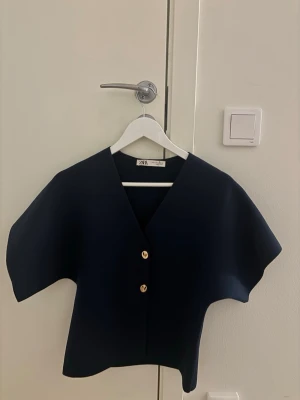 Mörkblå kortärmad topp från Zara - Stilren mörkblå topp från Zara med v-ringning och två guldknappar framtill. Den är stilren och funkar till mycket!