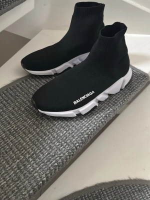Svarta skor  - Svarta  Speed Trainer sneakers med vit sula och stickad ovandel i stretchigt tyg. Strömlinjeformad design med högt skaft och tydlig logga på sidan. Skorna har chunky, sportig sula och en modern siluett som sticker ut.