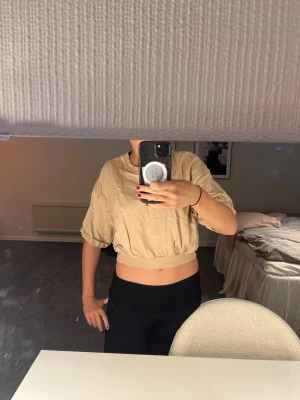 Beige croppad topp med kort ärm - Snygg beige croppad topp med korta ärmar och resår i midjan. Toppen har en loose passform och är tillverkad i ett lätt bomullsmaterial, perfekt för varmare dagar. Enkel och stilren design som passar till många outfits. Pris kan diskuteras!!🫰