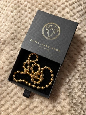 Vackert, helt nytt äkta guldhalsband från Emma Israelsson - 🤩 Exklusivt och helt oanvänt äkta guldpläterat halsband från designern Emma Israelsson. Tidlös stil. Kommer i originalask och med tillhörande putsduk och informationshäfte. Ursprungspris: 1.699 kr. Fantastisk kärleksgåva eller födelsedagspresent när någon tjej/kvinna i ditt liv fyller jämnt. 💝Endast urtaget för denna fotografering.  Fakta: Namn: Large Globe Chain Gold Necklace Mått: Kedjans längd är 50 cm.