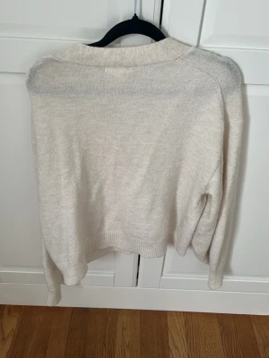 Beige stickad tröja från H&M - Mysig beige stickad tröja från H&M i storlek M. Tröjan har en avslappnad passform med långa ärmar och ribbade muddar vid ärmslut och nederkant. Perfekt för lager-på-lager och enkel att matcha med andra plagg.