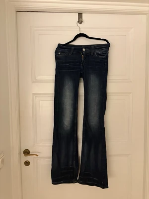 Mörkblå bootcut jeans - Snygga mörkblå bootcut jeans med lätt slitning framtill och klassiska fem fickor. Jeansen har en låg midja och vida ben, perfekta för en avslappnad och trendig look. Tillverkade i denim med stretch för extra komfort.