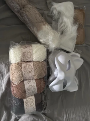 Cosplaykit, therian kit - Säljer ett cosplaykit med fyra nystan garn i färgerna vit, beige, ljusbrun och mörkbrun, en vit mask i plast samt ett par vita och bruna fuskpälsöron. Perfekt för att skapa en egen djur- eller fantasikaraktär till maskerad eller cosplay.
