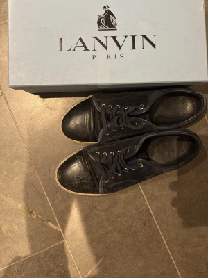 Svarta Lanvin sneakers i mocka och läder - Snygga blåa sneakers från Lanvin med ovandel i mocka. Skorna har vita gummisulor och klassisk snörning. Perfekta för dig som gillar stilrena och exklusiva sneakers med en lyxig känsla. Mycket liv i dessa kvar om de får en snabbresa till skomakaren