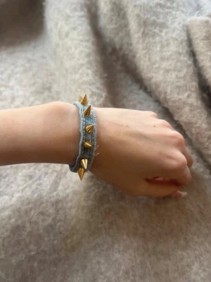 Blått armband med guldiga nitar - Coolt armband i ljusblått tyg med guldiga konformade nitar längs bandet.