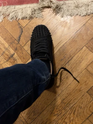 Loubotins svarta spikar - Säljer ett par svarta sneakers med coola nitar på tån. Skorna har snörning och är i mockaliknande material. Perfekta för dig som vill sticka ut med din stil och gillar detaljer som syns.