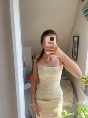 Champagnefärgad satinklänning med smala band - Jätte fin satin klänning som jag hade på mitt val förra året. Lite skrynklig på bilden. Har en jätte fin öppen rygg. Skriv privat för fler bilder!