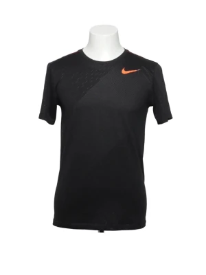 Svart Nike tränings-tshirt - Svart tränings-tshirt från Nike med orange logga på bröstet. T-shirten har rund halsringning, korta ärmar och är tillverkad i ett lätt och ventilerande funktionsmaterial. Perfekt för träning och sportaktiviteter.