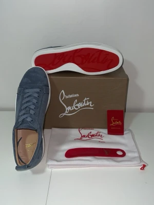 Blåa Christian Louboutin sneakers - Snygga blåa sneakers från Christian Louboutin i mocka med klassisk röd sula och vita kanter. Skorna har lågt skaft, matchande blåa skosnören och diskret branding på insidan. Perfekta för dig som vill sticka ut med exklusiva detaljer och lyxig känsla.