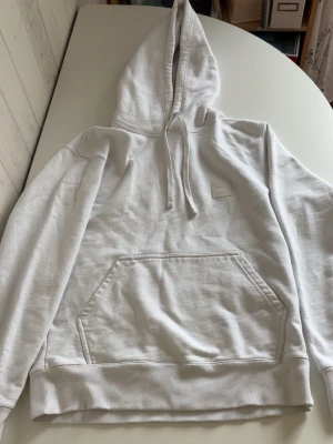 Vit hoodie från Neuw - Säljer en stilren vit hoodie från Neuw med klassisk huva och dragsko. Stor känguruficka framtill och ribbade muddar vid ärmslut och nederkant. Liten diskret logotyp på bröstet. Perfekt för en clean och avslappnad look.
