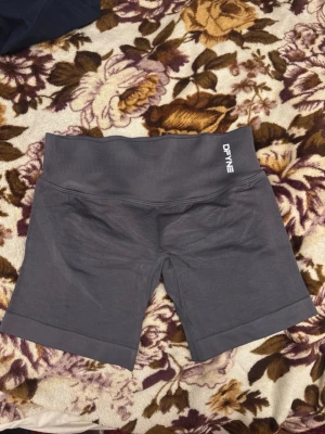 Grå träningstights shorts från DFYNE - Snygga grå träningstights shorts från DFYNE med hög midja och tight passform. Tillverkade i ett stretchigt material som passar perfekt för gym eller annan träning. Diskret logga framtill och baktill i midjan. Stilrena och bekväma för aktiva dagar.