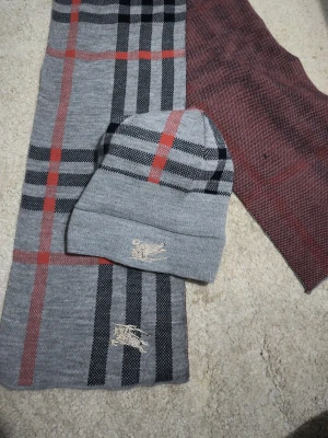 Grå och röd halsduk från Polo Ralph Lauren - Snygg halsduk i grått och rött med klassiskt rutmönster och broderad Polo Ralph Lauren-logga. Halsduken är mjuk och har en stilren design som passar perfekt till jackan. Materialet känns som en blandning av ull och akryl.