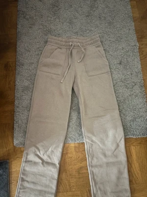 Beige mjukisbyxor med dragsko - Säljer ett par beige mjukisbyxor med raka ben och bred resår i midjan. Byxorna har stora fickor framtill  Perfekta för chill dagar och riktigt sköna att ha på sig. Materialet känns mjukt och bekvämt. Använda 2ggr