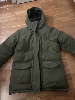 Olivgrön parkajacka Peak Performance - Säljer en olivgrön parkajacka från Peak Performance med huva och stora fickor framtill. Jackan är tillverkad i slitstarkt material och har en klassisk, rak passform. Perfekt för kalla dagar och outdoor-aktiviteter.