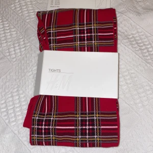 Rödrutiga tights från H&M - Snygga röda tights från H&M med klassiskt rutigt mönster i svart, vitt och gult. Perfekta för att addera lite färg till din outfit. Tightsen har elastiskt material för skön passform och är tunna och mjuka.