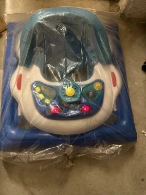 Blå babywalker med aktivitetsbord - Säljer en blå babywalker med aktivitetsbord som har flera färgglada knappar och lampor. Gåstolen är tillverkad i plast och har en stabil ram samt ett säte i blått. Perfekt för små barn som vill utforska och leka.