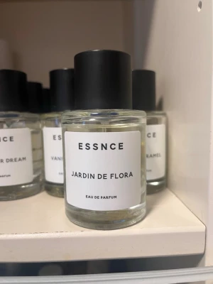 ESSNCE Jardin de Flora parfym - Fräsch Eau de Parfum från ESSNCE med namnet Jardin de Flora. Flaskan är cylindrisk i genomskinligt glas med svart rund kork och vit etikett med svart text. Doften ger en elegant och modern känsla, perfekt för dig som gillar blommiga toner.