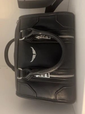Svart trendig handväska  - Jätte snygg svart väska köpt i Spanien. Säljer för att den aldrig används. Super fint skick och det tillkommer ett längre band. Skriv innan du köper (Pris kan diskuteras)