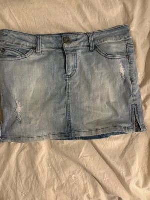 Lågmidjad jeanskjol  - Säljer en ljusblå jeanskjol från Only med slitna detaljer och dragkedja i sidan. Kjolen har klassisk femficksdesign, knappstängning och är i kort modell. Perfekt till sommaren och enkel att matcha med olika toppar. Kjolen är lågmidjad!! Passar XS/S