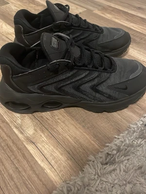 Svarta Nike sneakers med zigzag-mönster, Nike tw airmax  - Säljer ett par svarta Nike sneakers med coolt zigzag-mönster på sidan och chunky sula med håldetaljer. Skorna har mesh och syntetmaterial, samt svarta skosnören och diskret Nike-logga på sidan. Perfekta för dig som gillar sportig och modern stil.