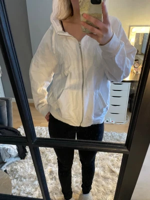 Vit hoodie med dragkedja - Säljer en vit hoodie med dragkedja framtill och huva med dragsnören. Hoodien har ribbade muddar vid ärmslut och nederkant samt två fickor fram. Perfekt för en avslappnad och enkel stil. Använd typ en gång, nypris 300kr eller 400kr. FRÅN BIKBOK. Ej bra pris,,, skriv till mig. Vill bli av med tröjan