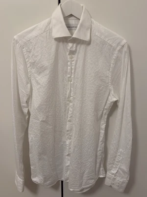 Vit skjorta från These Glory Days - Klassisk vit skjorta från These Glory Days med lång ärm och knappar framtill. Skjortan har en krispig struktur och är tillverkad i bomull. Perfekt för en clean och stilren look. Storleken är S/(37/38). 