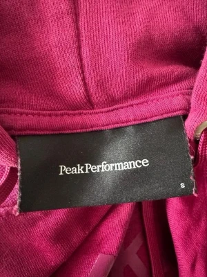 Vinröd  hoodie från Peak Performance S - Säljer en vinröd  hoodie från Peak Performance i mjukt bomullsmaterial. Hoodien har en klassisk huva och ribbade muddar vid ärmslut och nederkant. Perfekt för en avslappnad och sportig stil.