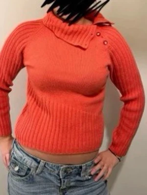 Korallröd stickad tröja med krage - Säljer en korallröd stickad tröja med hög krage och knappdetaljer vid halsen. Tröjan har ribbstickad struktur, långa ärmar och en något kortare passform. Perfekt för dig som vill ha en färgklick i garderoben! Köpt nyskick secondhand så det står ingen storlek. Skulle säga att det är en xs/s.