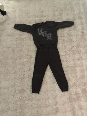 Mörkgrå loungewear-set från Benetton 98-104  - Ett mörkgrått/antracitfärgat mjukisset bestående av en sweatshirt och ett par matchande byxor. Lagning i grenen men fint skick i övrigt. Rök och djurfritt hem, passar 3-4 åringar.