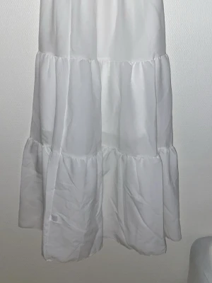 Vit volangkjol - Säljer en lång vit kjol med flera volanger och luftig passform. Kjolen är sydd i ett mjukt tyg och har en avslappnad, flowy stil som passar perfekt till olika outfits. Enkel att matcha och superfin till sneakers eller boots. Har aldrig haft på mig den och är helt ny!