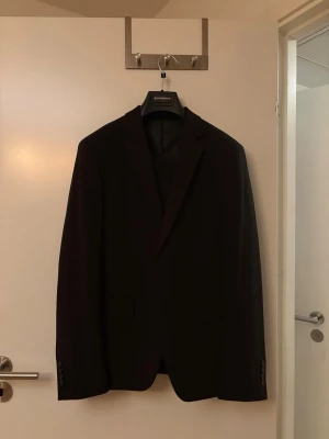 Svart kostym från Lindbergh White - Stilren svart kostym från Lindbergh White i slim fit-modell. Klassisk design med smala slag och två framfickor. Perfekt för dig som vill ha en enkel och snygg kostym till många olika tillfällen.