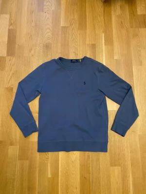 Blå sweatshirt från Ralph Lauren - Mörkblå sweatshirt från Polo Ralph Lauren med    broderad logga på bröstet. Tröjan har långa ärmar, ribbade muddar och är tillverkad i mjuk bomull. Enkel och stilren design som passar till det mesta. Den är använd fåtal gånger, väldigt bra skick.