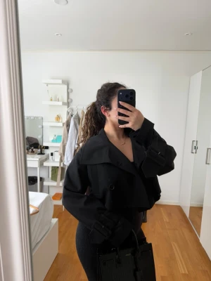 Svart cropped trenchcoat från Avora strlk 36 - Svart cropped trenchcoat i Strlk 36/S från Avora. Säljer för 1000kr. Toppskick. 