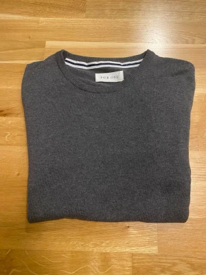 Mörkgrå stickad tröja Pier One - En stilren mörkgrå tröja från Pier One med rund halsringning och långa ärmar. Tröjan har ribbade muddar vid ärmslut och nederkant. Perfekt för lager på lager och enkel att matcha med olika outfits.