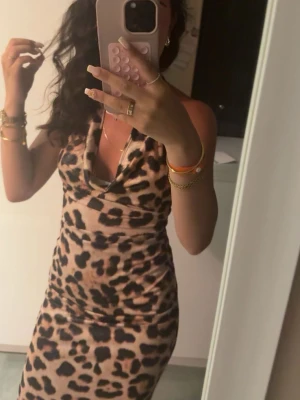 Leopardmönstrad långklänning - Säljer en snygg långklänning med leopardmönster och draperad urringning. Klänningen är ärmlös och har öppen rygg, vilket ger en trendig och cool look. Perfekt för dig som vill sticka ut med ett djuriskt mönster. Materialet känns mjukt och följsamt.