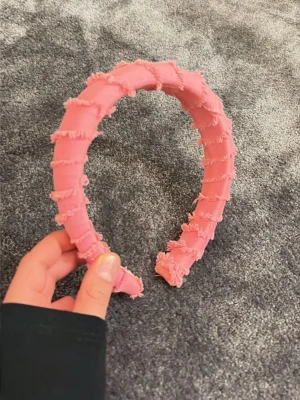 Rosa diadem med fransiga detaljer - Säljer ett fluffigt rosa diadem med fransiga tygdetaljer som ger en cool och trendig look. Diademet är vadderat och har en bred form som sitter bekvämt på huvudet. Perfekt för att lyfta vilken outfit som helst med en poppig färg. Tyvärr lite smink på men ingenting som syns. 