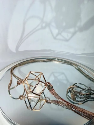 Roséguld halsband med kristall - Ett långt, elegant halsband i roséguldfärgad metall med ett unikt hänge. Hänget består av en geometrisk "bur" som omsluter en fasettslipad kristall  Skick: Halsbandet är använt och har blivit lite "rostigt" på vissa ställen (se bilder). Därav det låga priset.