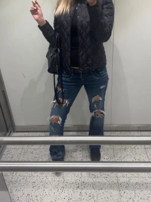 Blå slitna jeans med hål - Säljer ett par blå jeans med rejält slitna detaljer och stora hål över knän och lår. Jeansen har en klassisk femficksmodell och är i rak passform. Perfekta för en avslappnad och trendig streetstil.