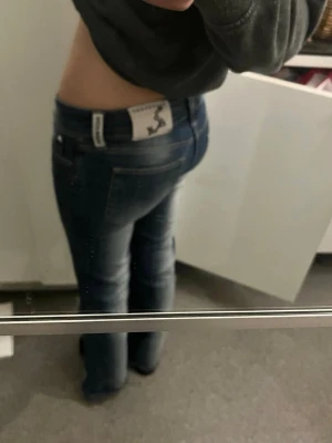 Blå bootcut-jeans - Snygga blå bootcut-jeans, med klassisk femficksdesign och ljusa slitningar framtill. Jeansen har låg midja och en figurnära passform upptill som går ut i ett lätt utsvängda ben.
