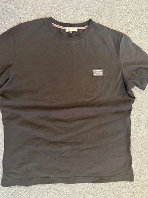 Svart Burberry t-shirt med logga - Svart t-shirt från Burberry med klassisk rund hals och en snygg patch med Burberry London England på bröstet. Den är 68cm på längden och 57cm på brädden 