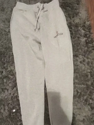 Grått loungewear-set från Moncler - Säljer ett grått loungewear-set från Moncler med matchande sweatshirt och byxor. Setet har en avslappnad passform, dragsko i midjan på byxorna och Moncler-logga på både tröjan och byxan. Perfekt för chill dagar hemma eller när du vill vara bekväm men ändå snygg.