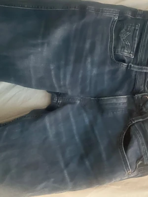 Mörkblå jeans med klassisk passform replay - Snygga mörkblå jeans med klassisk 31w 34L femficksdesign och diskreta slitningar. Jeansen har raka ben och normal midja, perfekta för en avslappnad stil. Materialet är mjukt och bekvämt, vilket gör dem till ett självklart val i garderoben.