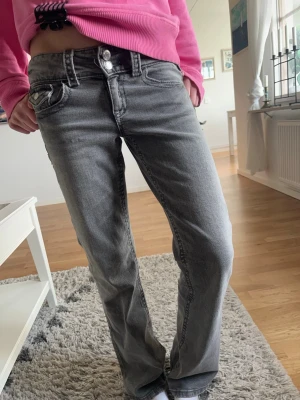 Grå utsvängda jeans med dubbla knappar - Snygga grå jeans med utsvängda ben och dubbla knappar i midjan. Jeansen har klassiska fem fickor och en tvättad look som ger en avslappnad vibe. Perfekta för dig som gillar en enkel men trendig stil.