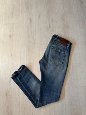 Replay Jeans - Snygga blå slim fit jeans från Replay med slitningar och lätt tvättad look. Jeansen har klassisk femficksdesign, läderpatch bak och detaljerade sömmar. Perfekta för en avslappnad och trendig stil.