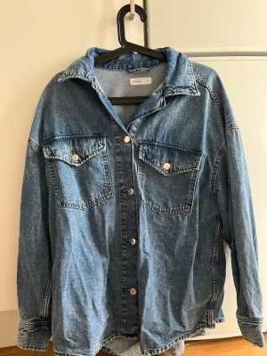 Oversized blå jeansjacka Perfect Jeans - Snygg oversized blå jeansjacka från Perfect Jeans. Klassisk modell med två stora bröstfickor med lock och silverfärgade knappar. Tillverkad i slitstarkt denimtyg och har en avslappnad passform med nedhasade axlar.